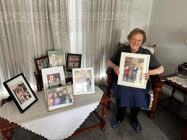 Asimo Nikolakopoulos holding a photograph of her grandchildren, Joanna, Adriana and Yannis Halias, and her daughter, Sophie Halias, 2023.