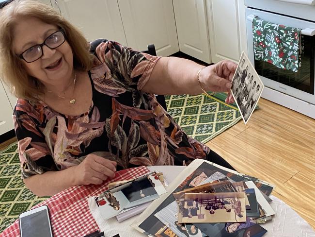 a woman with glasses holds out photos to the camera