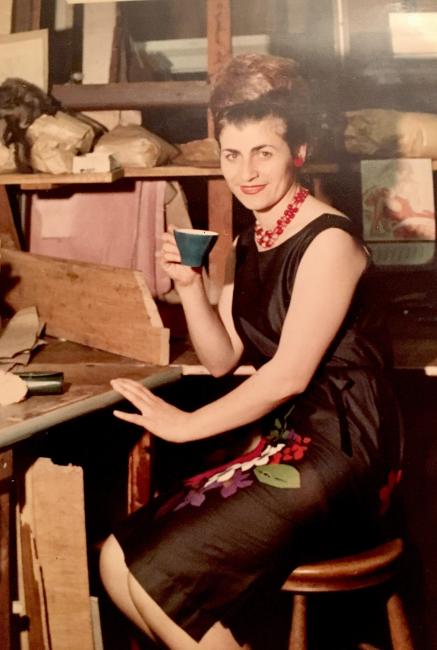 Woman sitting drinking tea at a workbench.